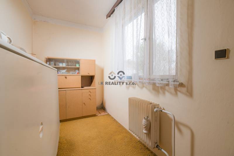Szoba egy családi házban régebbi bútorokkal, radiátorral és szőnyeggel.