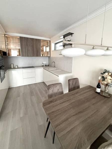 Konyha egy kétszobás lakásban fa mintázatú padlóval, világos belső térrel és étkezőasztallal.