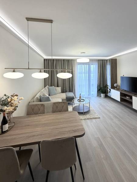 Nappali étkezőasztallal, kanapéval és fa dekorációjú padlóval egy kétszobás lakásban.