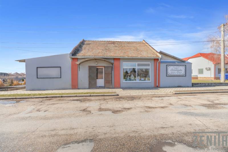 Kereskedelmi helyiségek Okoč városában kirakatokkal és ferde tetővel.