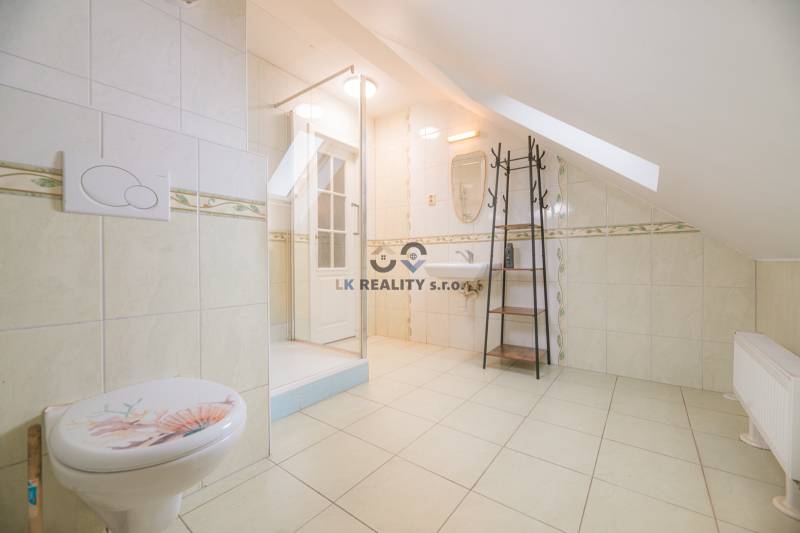 Fürdőszoba WC-vel, zuhanyzóval és mosdóval egy tetőtéri kétszobás lakásban.