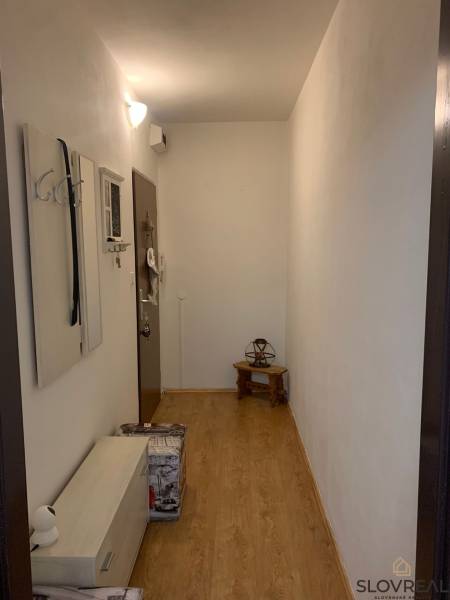 Keskeny előszoba fehér falakkal, fa hatású padlóval és minimalista bútorokkal.