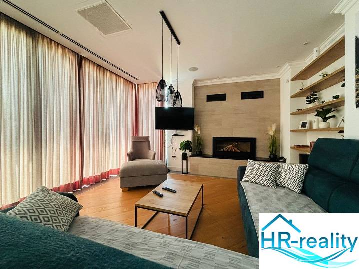 Nappali a villában kandallóval, TV-vel, fa hatású padlóval és kényelmes ülőgarnitúrával.