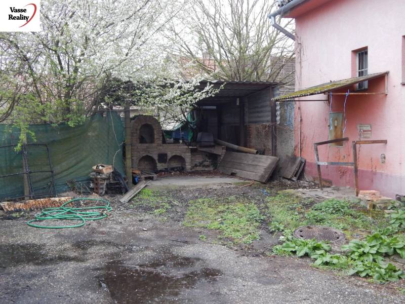 Kültér a gasztronómiai helyiségekben Búcsban, régi kemencével és tavaszi növényzettel.