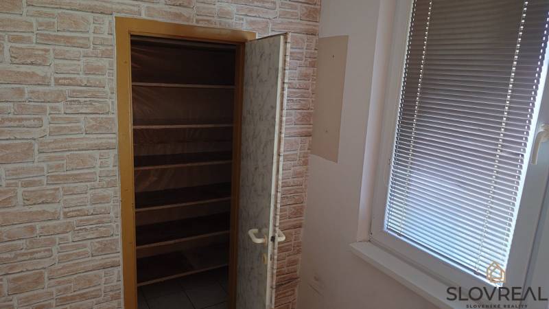 Szekrény polcokkal az ablak mellett egy kétszobás lakásban, téglafal utánzatú tér.