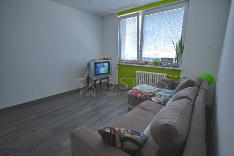 Nappali egy egyszobás lakásban fa mintás padlóval és régebbi televízióval.