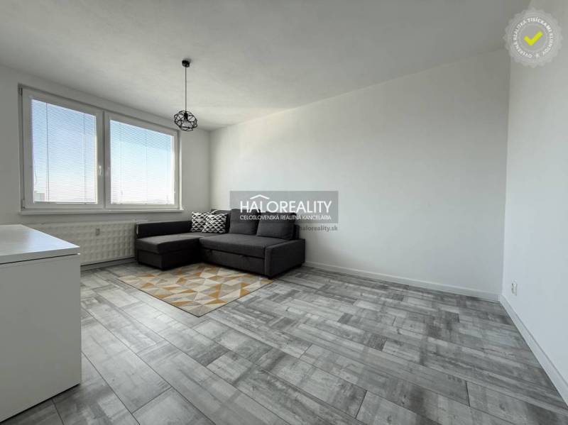 Nappali egy kétszobás lakásban, fa mintázatú padlóval és szürke kanapéval.