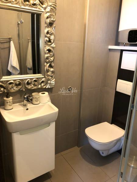 Fürdőszoba egy kétszobás lakásban, időtlen tükörrel, mosdóval és fali WC-vel.