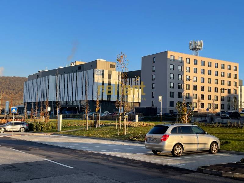 Épületek a Dominika utcában, Lamačban, Pozsonyban, parkolóval körülvéve és dombokkal a háttérben.