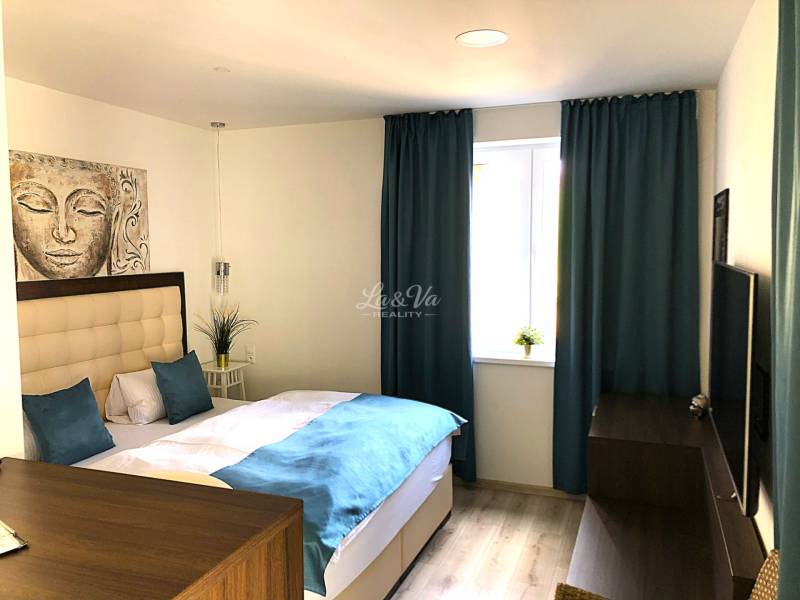 Garzonlakás világos bútorokkal, ággyal és kék függönyökkel, fa dekoros padlóval.