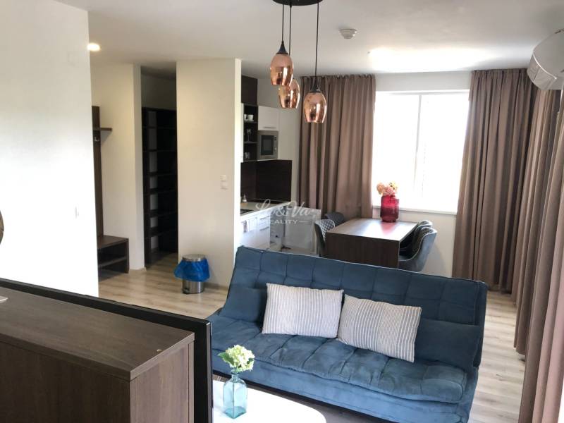 Nappali egy kétszobás lakásban kanapéval és étkezőasztallal; fa dekoros padló.