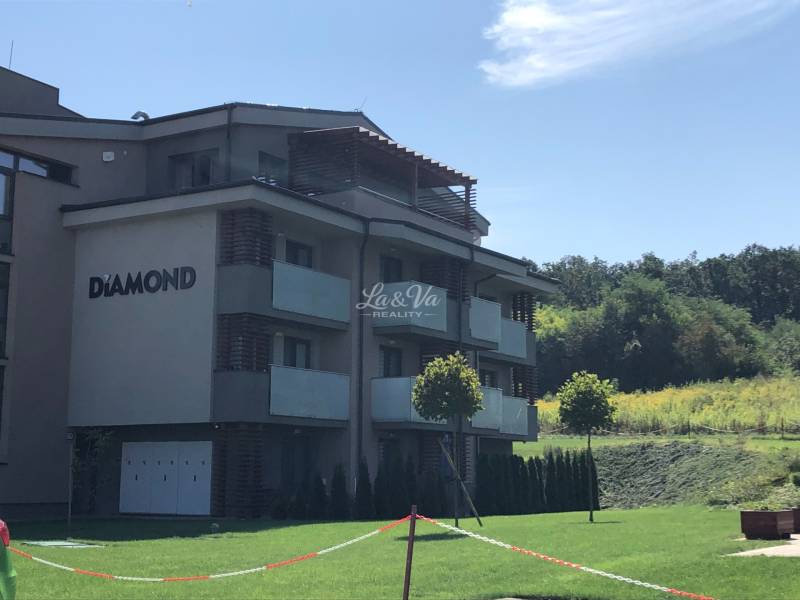 Kétszobás lakás épülete Podhájska településen, zölddel körülvéve és felhőtlen égbolttal.