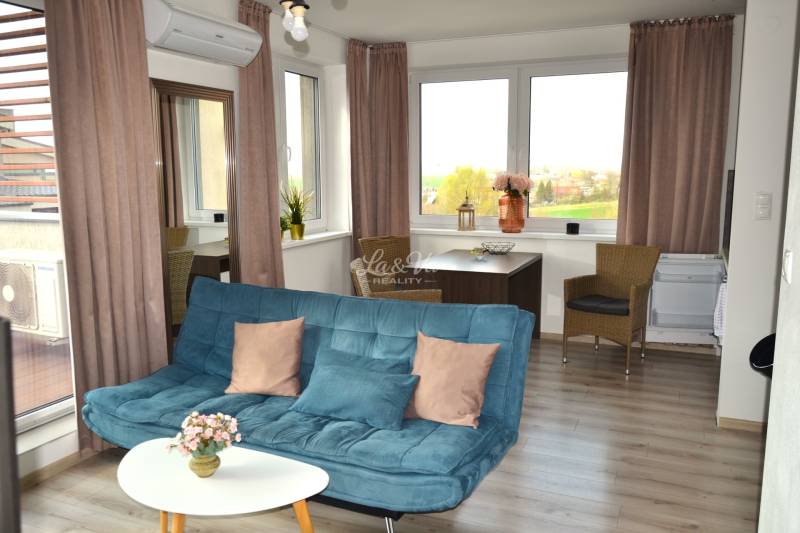 Nappali kanapéval, asztallal, növényekkel és fa dekorációjú padlóval egy kétszobás lakásban.