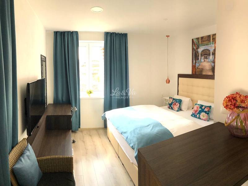 Világos szoba egy 2 szobás lakásban kék függönyökkel és fa mintázatú padlóval.