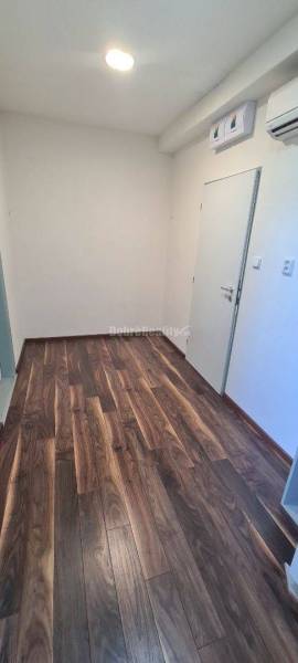 Irodai folyosó fa mintázatú padlóval és fehér falakkal.