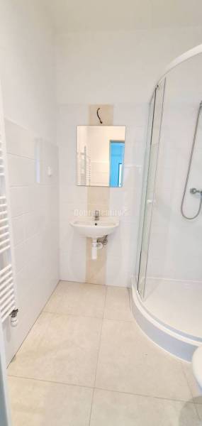 Fürdőszoba mosdóval, zuhanyzóval és fehér csempékkel az irodában.