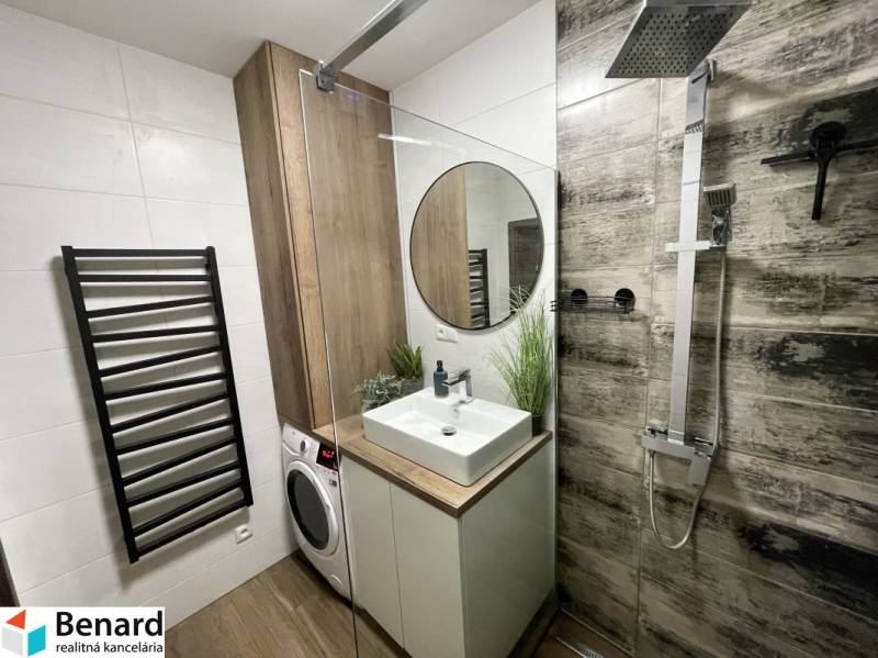 Fürdőszoba egy kétszobás lakásban mosdóval, zuhanyzóval és mosógéppel, fa dekoros padlóval.