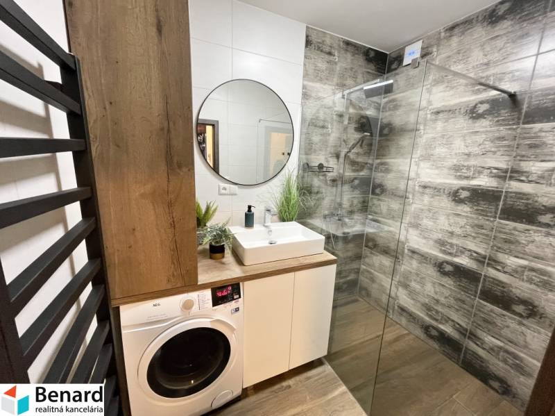 Fürdőszoba zuhanyzóval, mosdóval, mosógéppel és fa dekorációjú padlóval egy kétszobás lakásban.