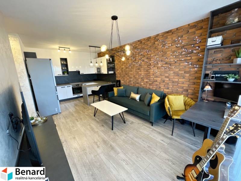 2 szobás lakás nappali része téglafallal, fa dekoros padlóval és konyhasarokkal.