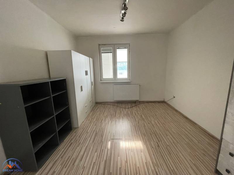 Egy szoba egy háromszobás lakásban fa dekorációjú padlóval és egyszerű berendezéssel.