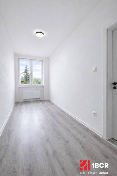 Keskeny szoba nagy ablakkal és fa dekorációjú padlóval egy háromszobás lakásban.