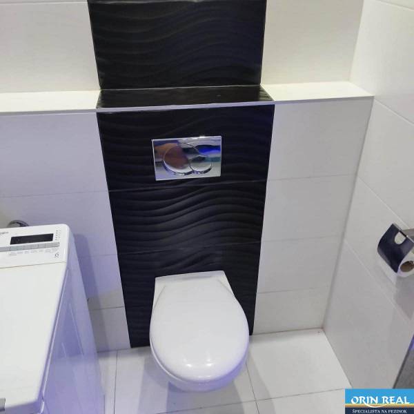 Fürdőszoba egy háromszobás lakásban WC-vel és mosógéppel, fekete csempékkel.