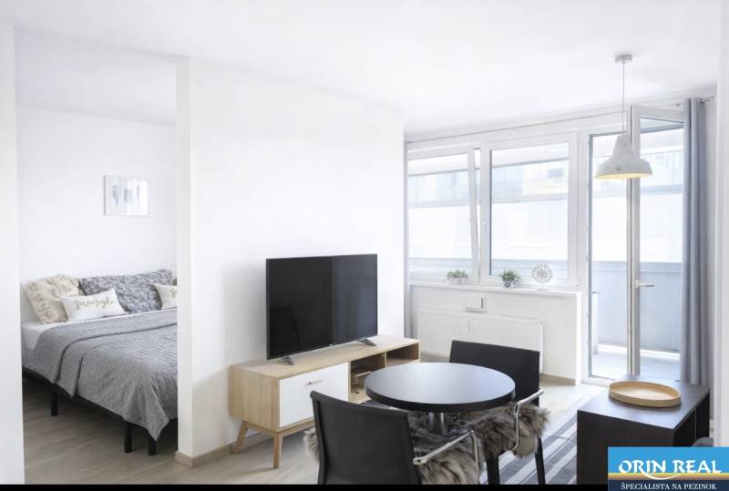 Világos nappali egy kétszobás lakásban, televízióval és étkezőasztallal.