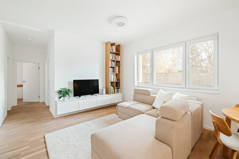 Világos nappali egy négy szobás lakásban, fa mintázatú padlóval, kanapéval és TV-vel.