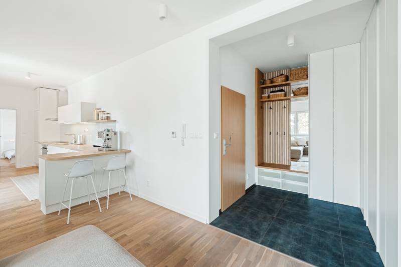 Négyszobás lakás előszobája fa mintázatú padlóval és konyhasarokkal.