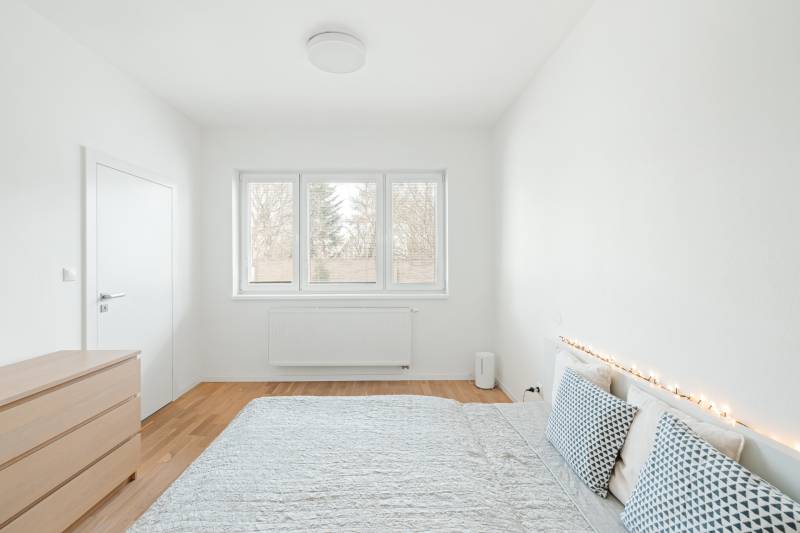 Világos hálószoba egy 4 szobás lakásban, fa dekor padlóval és dekoratív párnákkal.