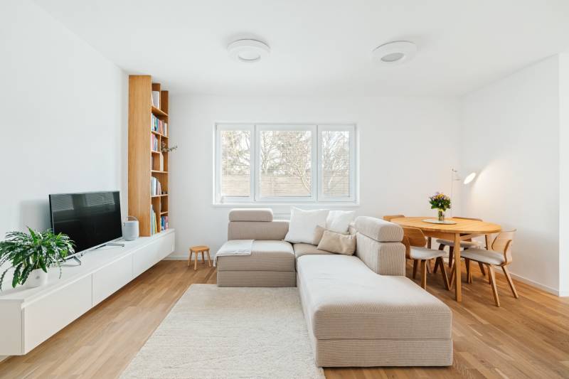 Nappali kanapéval, TV-vel, könyvespolccal és étkezőasztallal, fa dekoros padlóval.