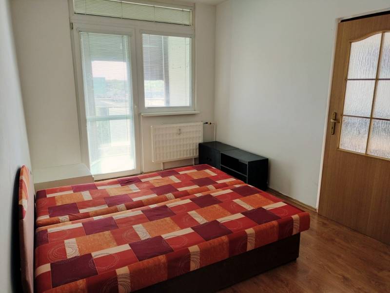 Hálószoba egy háromszobás lakásban, ággyal és fa dekorációjú padlóval.