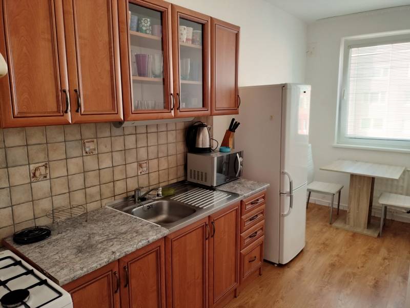 Konyha egy háromszobás lakásban, fa dekor padlóval és fa bútorokkal.