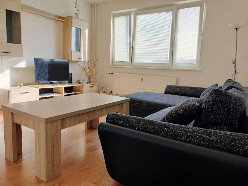 Nappali kanapéval, televízióval és fa mintázatú padlóval egy háromszobás lakásban.