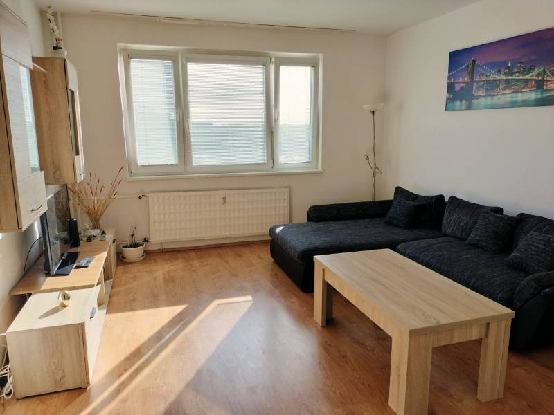 Nappali kanapéval, dohányzóasztallal és fa dekorációjú padlóval egy háromszobás lakásban.