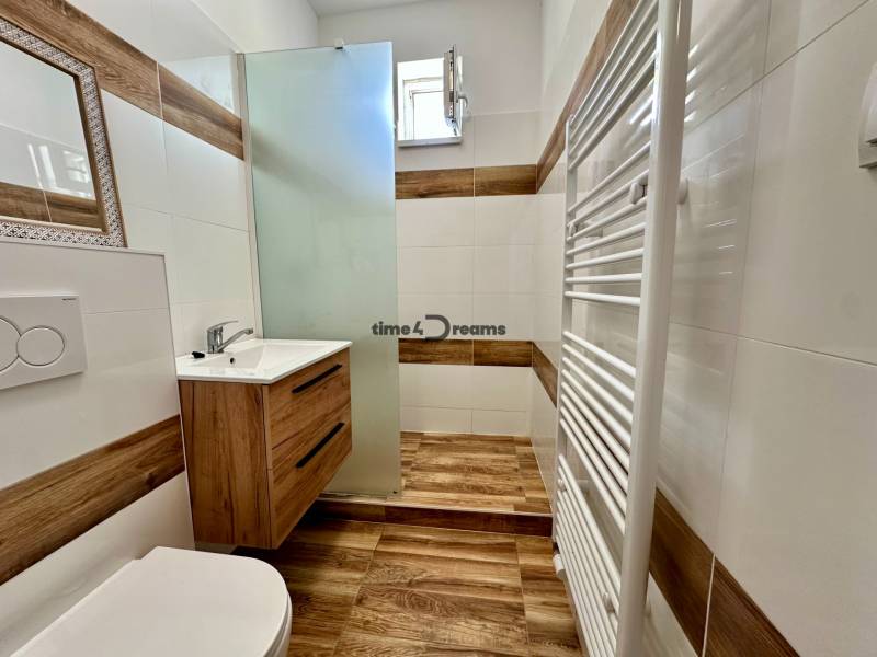 Fürdőszoba garzonlakásban fa mintás padlóval és csempével.