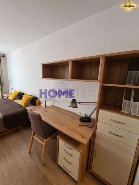 Íróasztal polcokkal, ágy és fa dekorációjú padló a kétszobás lakásban.