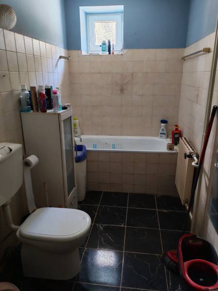 Fürdőszoba káddal és WC-vel egy családi házban, sötét csempével és ablakkal.
