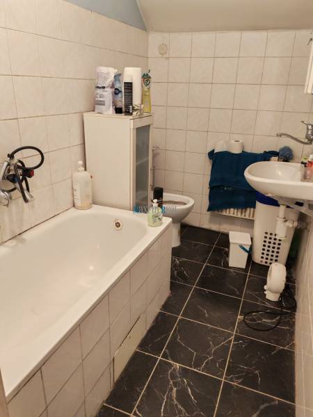 Fürdőszoba családi házban káddal, mosdóval és sötét mintás csempével.