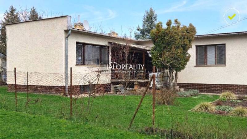 Családi ház Poltáron, gyep és fák veszik körül, terasszal és kerítéssel.