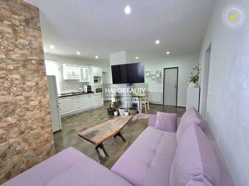 Családi ház nappalija kőburkolattal és konyhasarokkal.