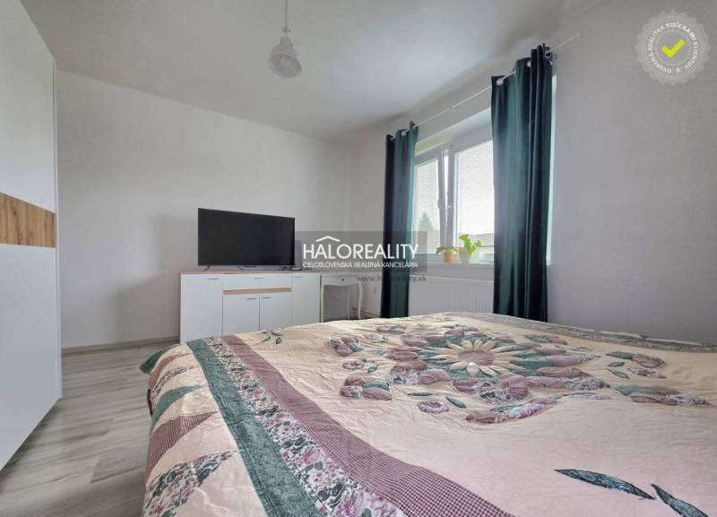 Hálószoba családi házban ággyal, televízióval és sötét függönyös ablakkal.