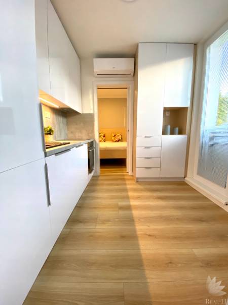 Világos konyha egy kétszobás lakásban, fa hatású padlóval és fehér szekrényekkel.