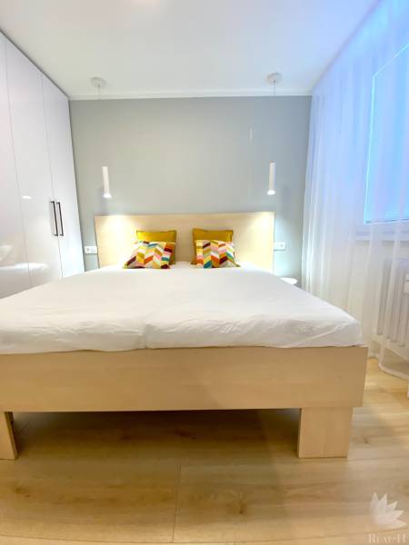 Világos hálószoba egy kétszobás lakásban színes párnákkal az ágyon.