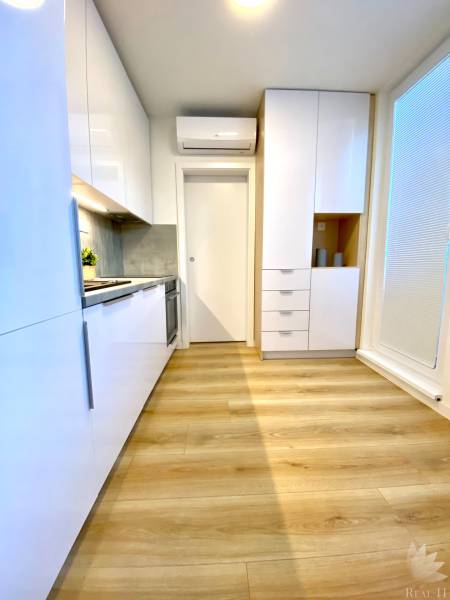 Konyha fehér szekrényekkel és fa dekor padlóval egy kétszobás lakásban.