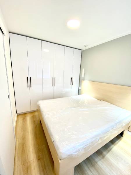 Hálószoba franciaággyal, fehér szekrénnyel és fa mintázatú padlóval egy kétszobás lakásban.