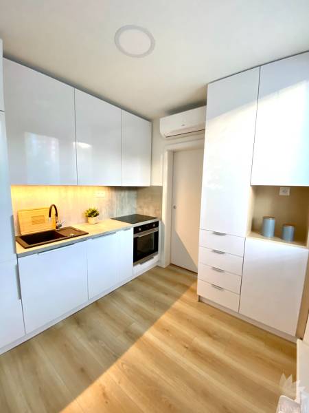 Konyha egy kétszobás lakásban fehér szekrényekkel és fa mintázatú padlóval.