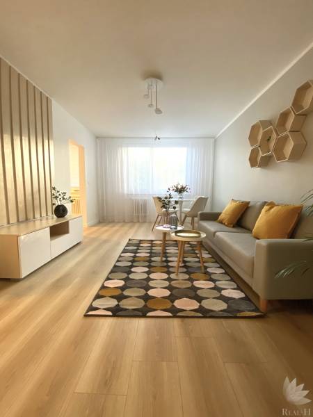 Nappali egy kétszobás lakásban, fa mintázatú padlóval és mintás szőnyeggel.