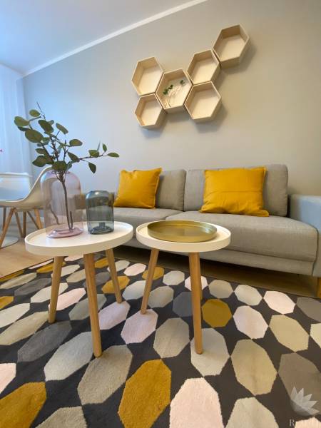 Nappali egy kétszobás lakásban geometrikus polcokkal, szürke kanapéval és színes szőnyeggel.