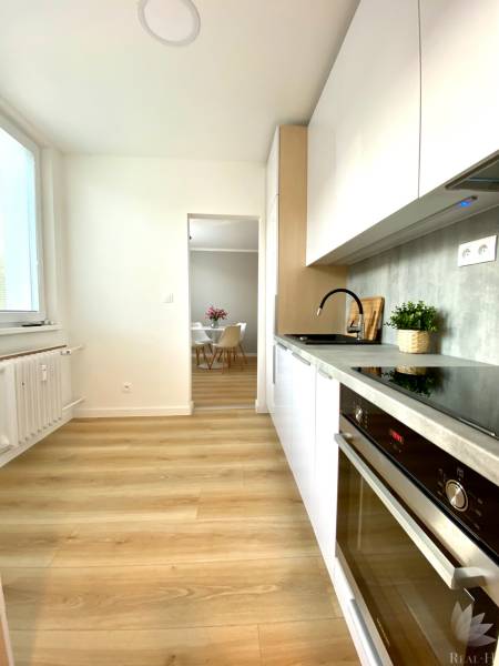 Konyha egy kétszobás lakásban fehér szekrényekkel és fa mintázatú padlóval.